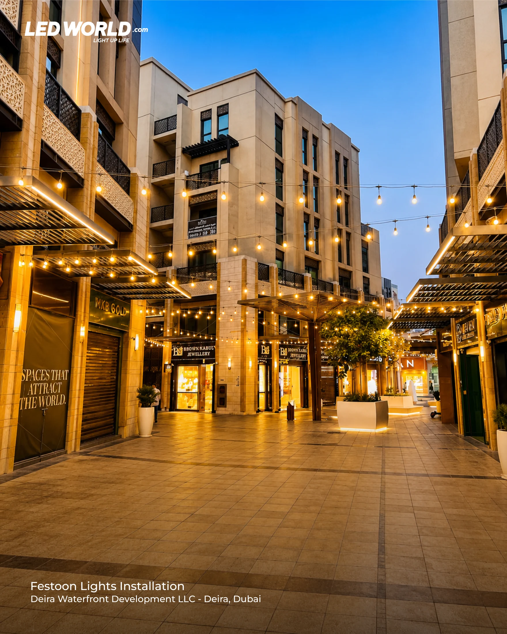 Wide view of overhead festoon strings and a paved pedestrian route in Deira at dusk